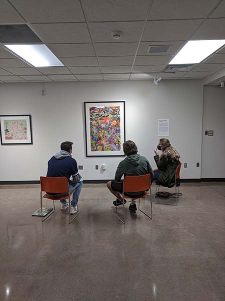 Three students sitting and looking at a colorful drawing by Frank Big Bear at the museum