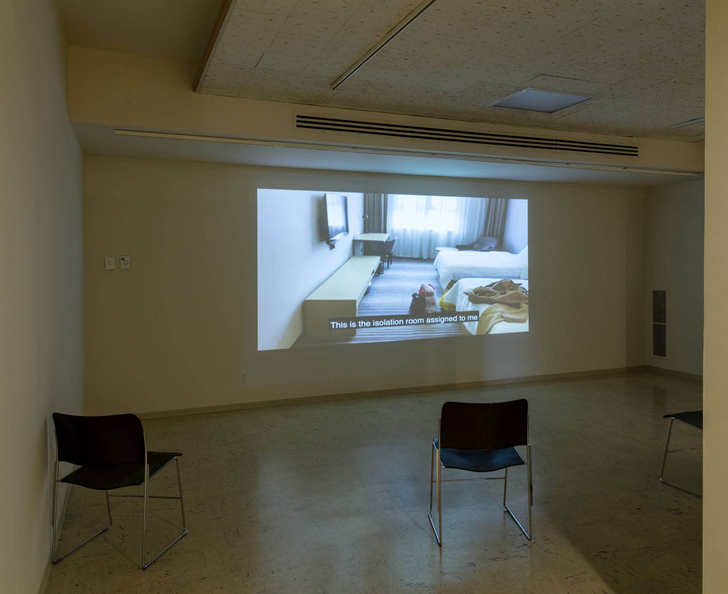 view of the museum's gallery showing the projection of a hotel room and two black chairs