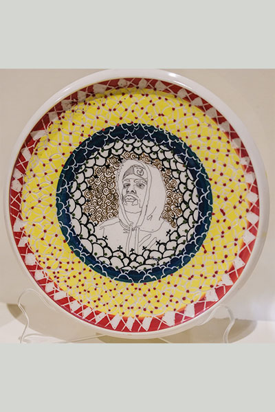 hooded male figure in the middle of a ceramics plate with blue, yellow and red colors