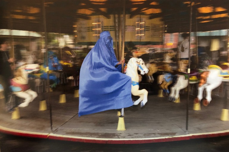 woman dressed in blue hijab riding white horse on a carousel