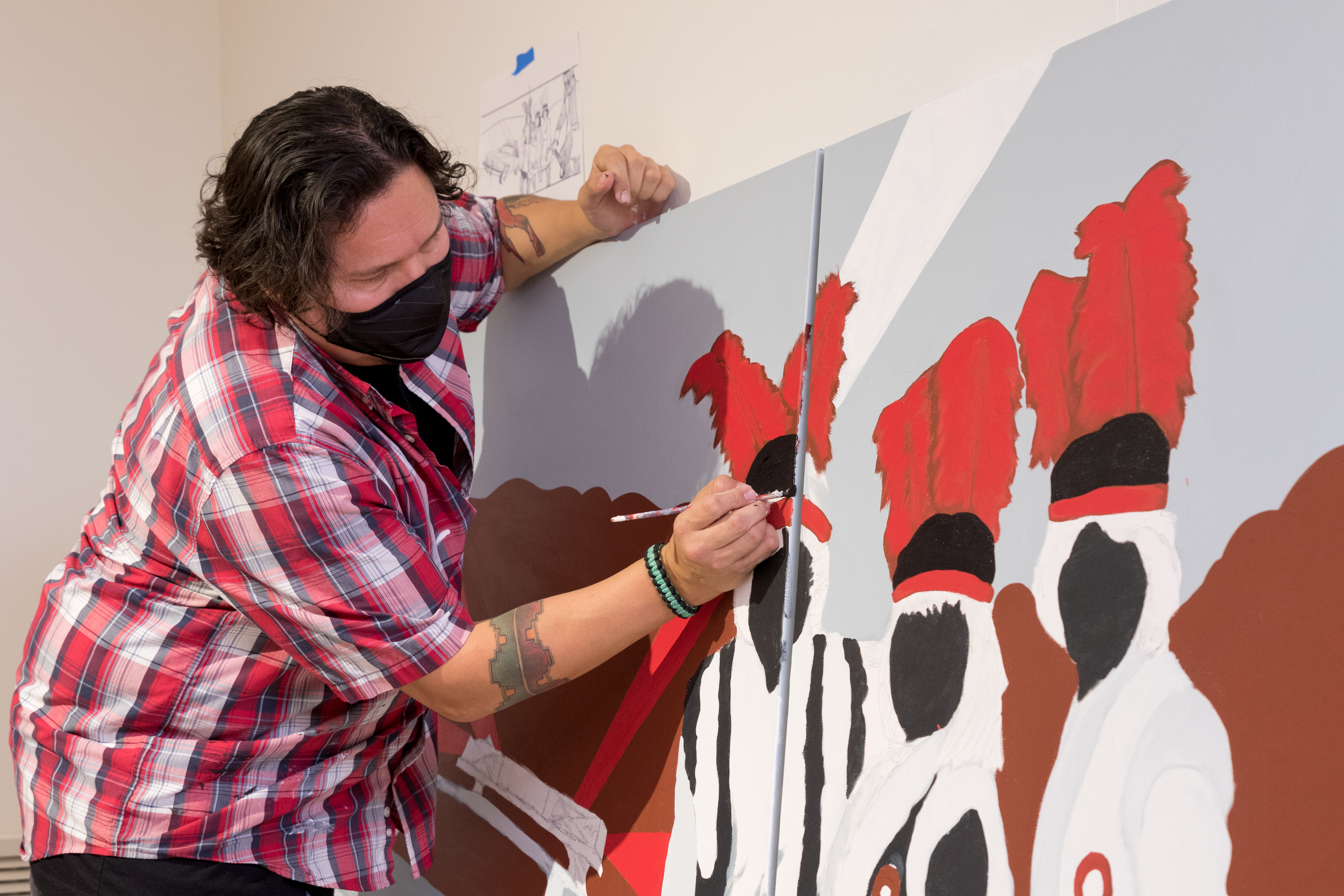 Artist Jonathan Thunder leaning by his canvas to paint his mural
