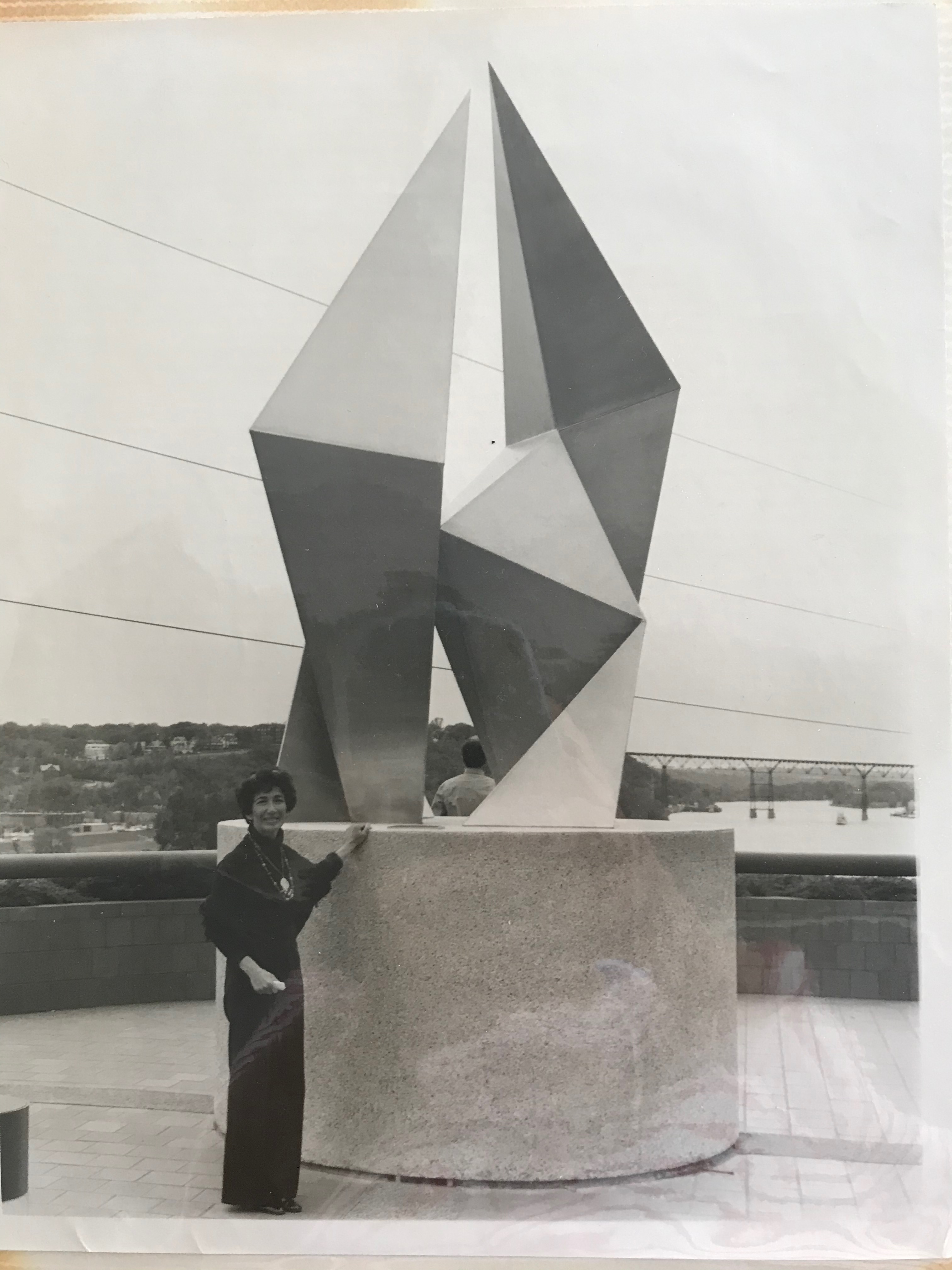 A black and white photo of woman standing next to a sculpture.