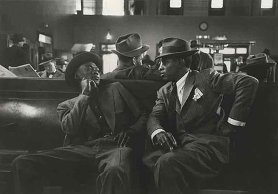 two African American men in suits sitting on a bench waiting for their greyhound bus