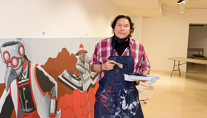 Johnathan Thunder with paintbrush in hand near his in-progress mural
